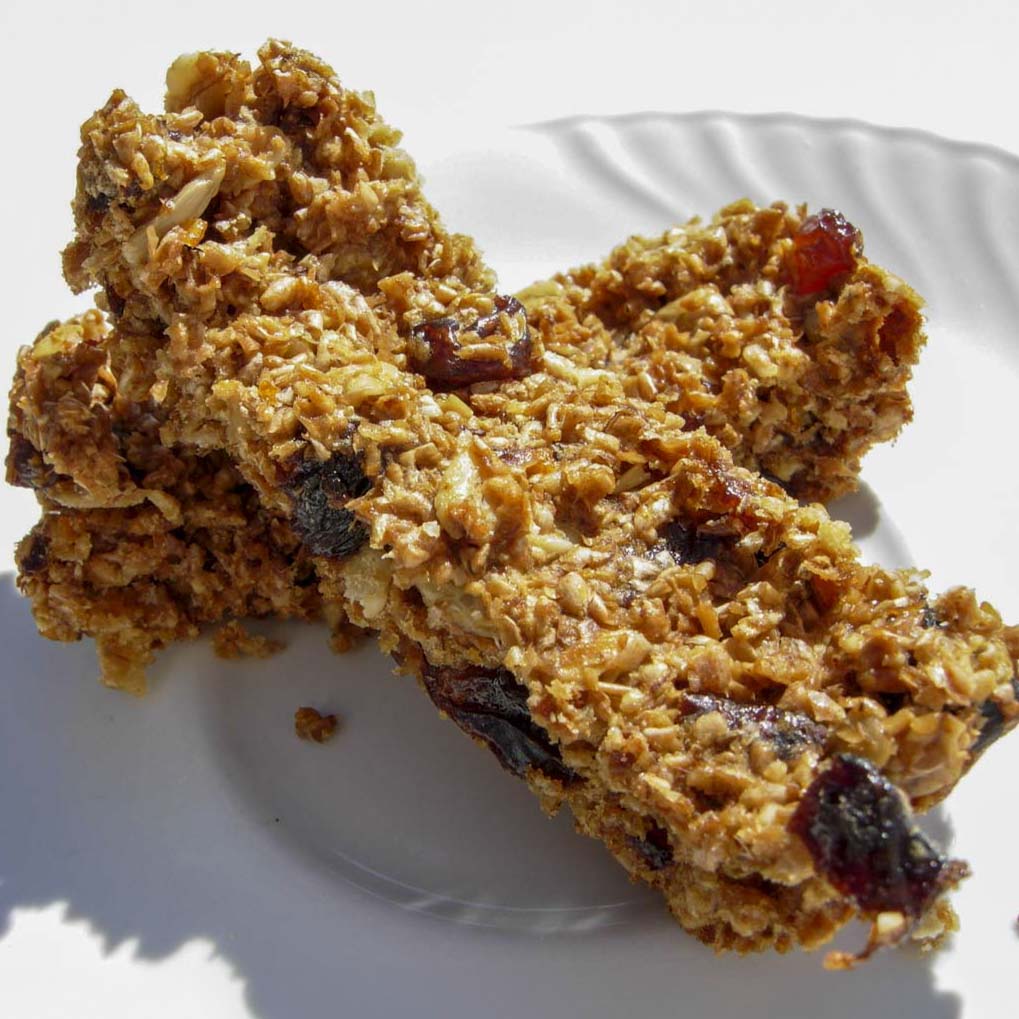 Barrette ai cereali fatte in casa con fiocchi di avena e frutta secca su piatto bianco