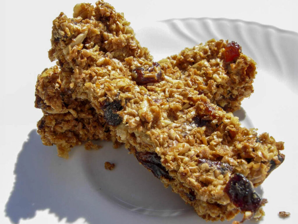 Barrette ai cereali fatte in casa con fiocchi di avena e frutta secca su piatto bianco