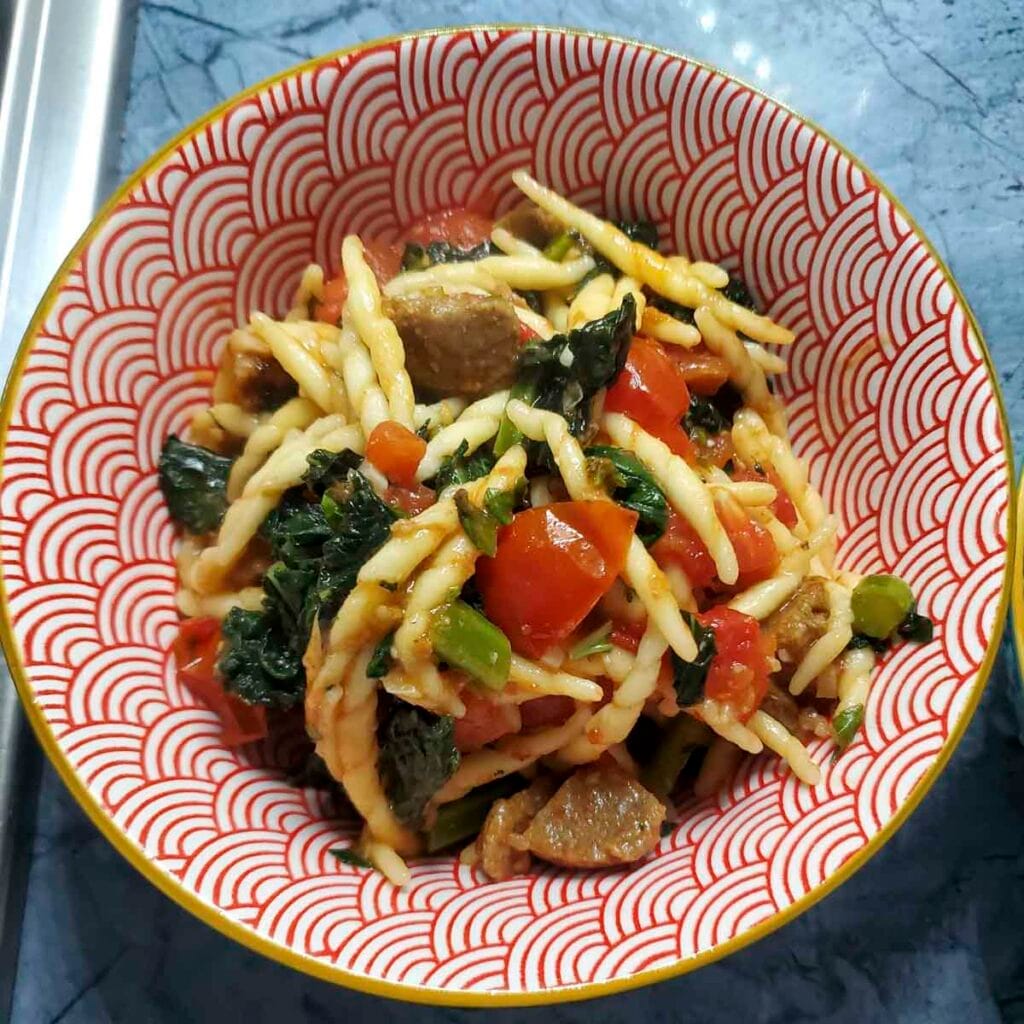 Pasta con trofie, cavolo nero e polpette vegetariane servita in un piatto fondo, con pomodorini freschi e basilico