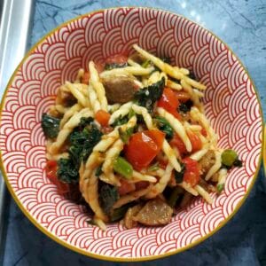 Pasta con trofie, cavolo nero e polpette vegetariane servita in un piatto fondo, con pomodorini freschi e basilico