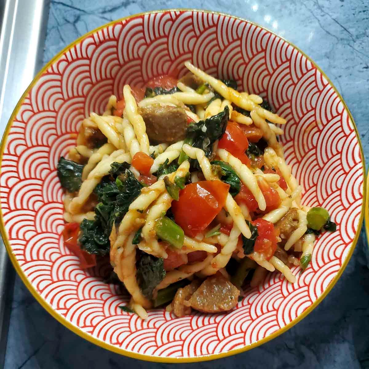 Pasta con trofie, cavolo nero e polpette vegetariane servita in un piatto fondo, con pomodorini freschi e basilico