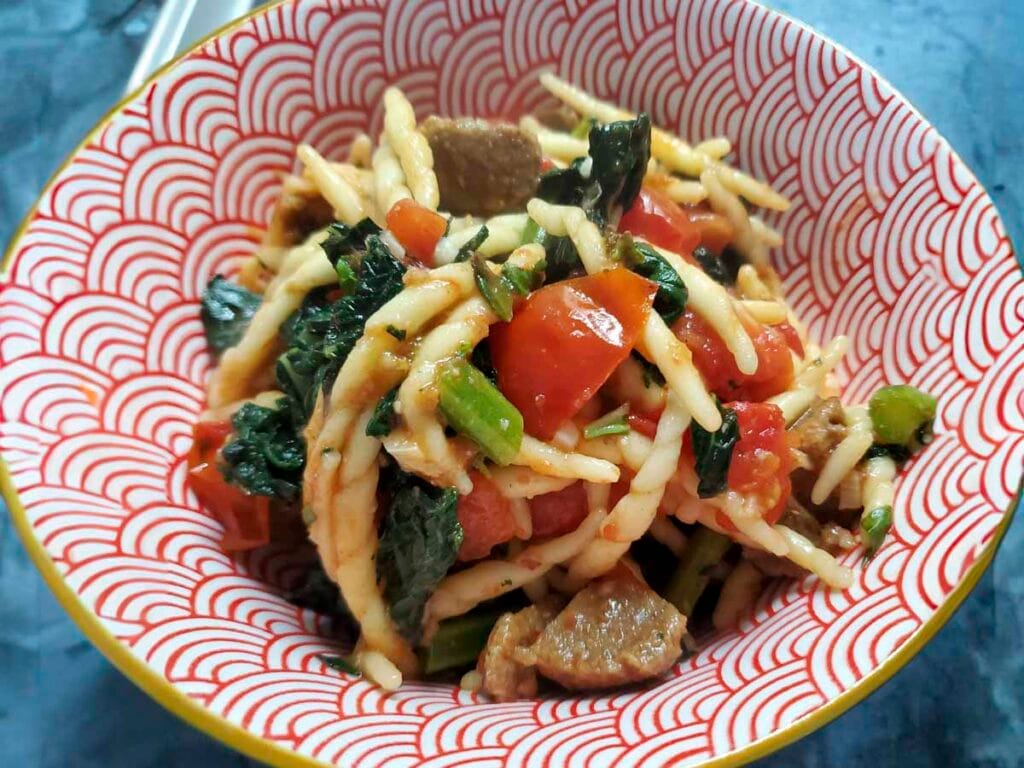 Piatto unico vegano con trofie, cavolo nero e polpette proteiche, decorato con foglie di basilico