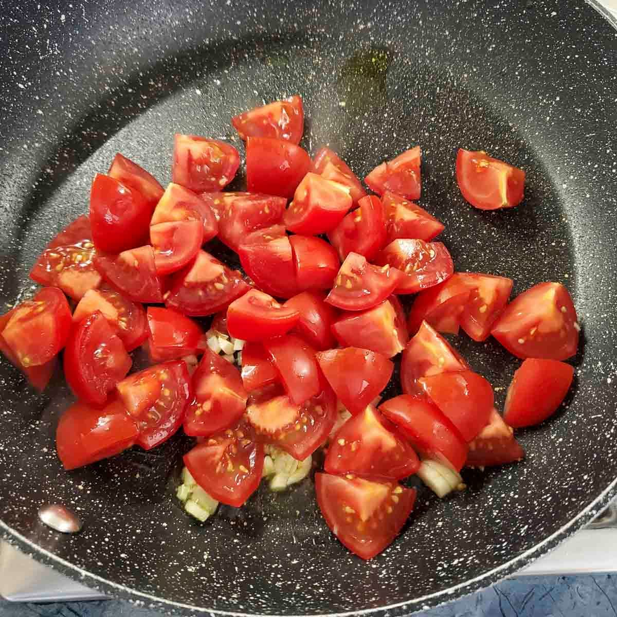 Pomodorini freschi tagliati a metà che cuociono nel soffritto