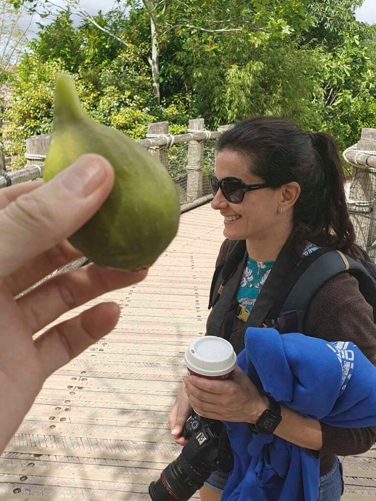 Donna di profilo con lunghi capelli scuri, in piedi tra alberi in un ambiente naturale.