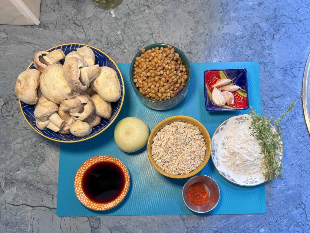Ingredienti per Hamburger vegani con funghi, lenticchie, avena, cipolla, aglio, farina, timo, paprika e salsa di soia.