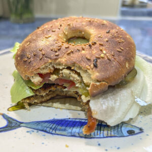 Hamburger vegano con funghi e avena servito in un bagel proteico con insalata, pomodoro e cetriolini.